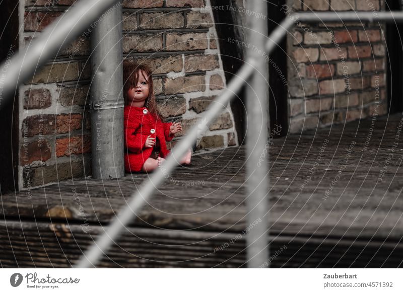 Red dressed doll sits lost on wooden floor with railing Doll Doomed Sit Fear Wood planks half-timbered brick Infancy loss Hiding place Loneliness Toys Child