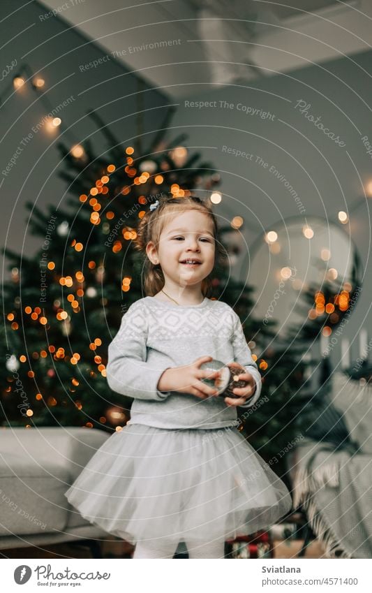 A beautiful little girl in a festive dress is standing at the Christmas tree. the concept of Christmas and New Year christmas holiday festive mood