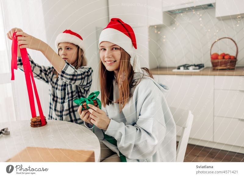 Two girls decorate cookies with bright red and green ribbons, prepare sweet treats for guests on Christmas or New Year's Eve gift christmas new year present