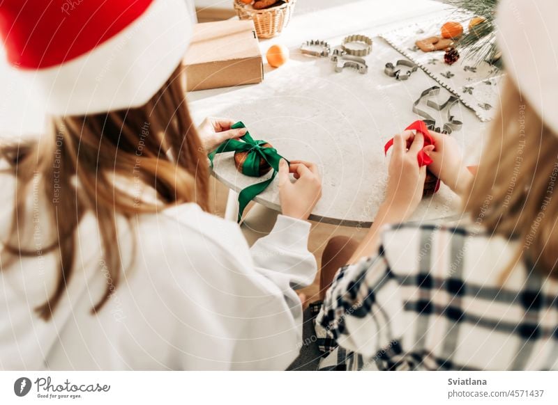 Two girls decorate cookies with bright red and green ribbons, prepare sweet treats for guests on Christmas or New Year's Eve gift christmas new year present