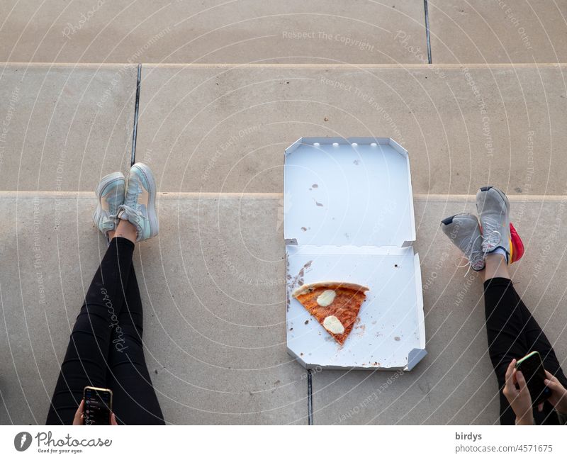 Pizza to go. Teenage girls playing on smartphone and eating pizza outside. Bird's eye view Youth (Young adults) pizza box free time at the same time sneakers