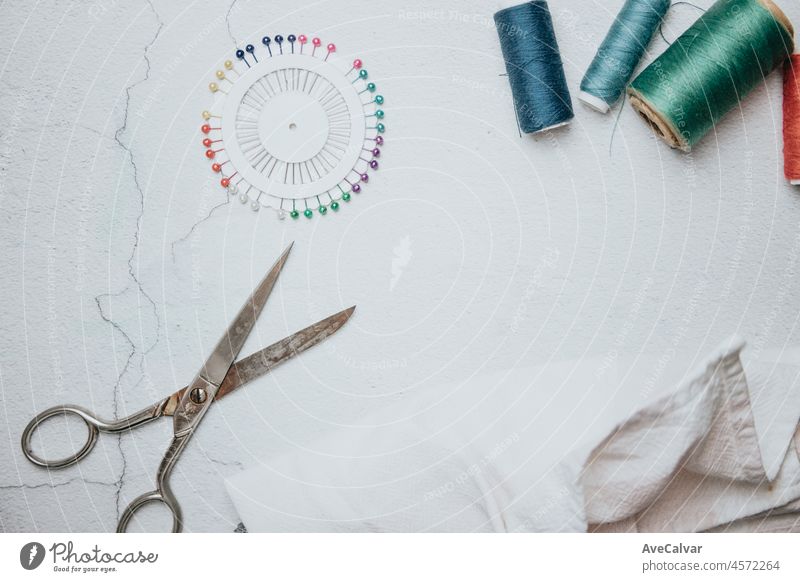 Flat lay composition with sewing accessories: threads, red and gray fabrics, scissors, buttons, set of needles, pins and other sewing tools on a white background. Top view, copy space, mock up.