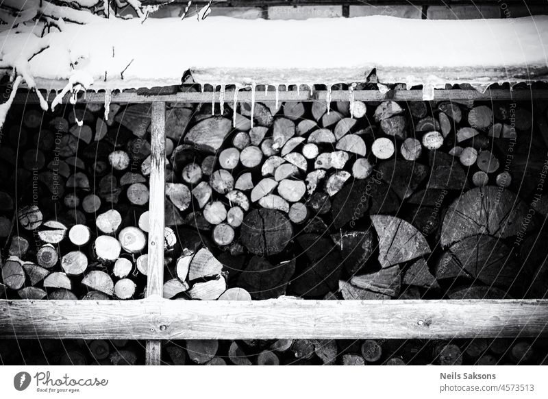firewood in winter under snow covered roof, icicles, black and white monochrome background branch brown chopped cold color cut energy environment fireplace