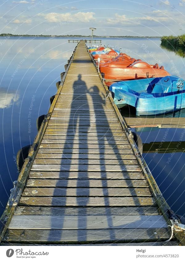 long shadows of two people on a jetty with pedal boats at the lake Shadow Human being Woman Child Footbridge wooden walkway Pedalo Lake Dümmer See Water Sky