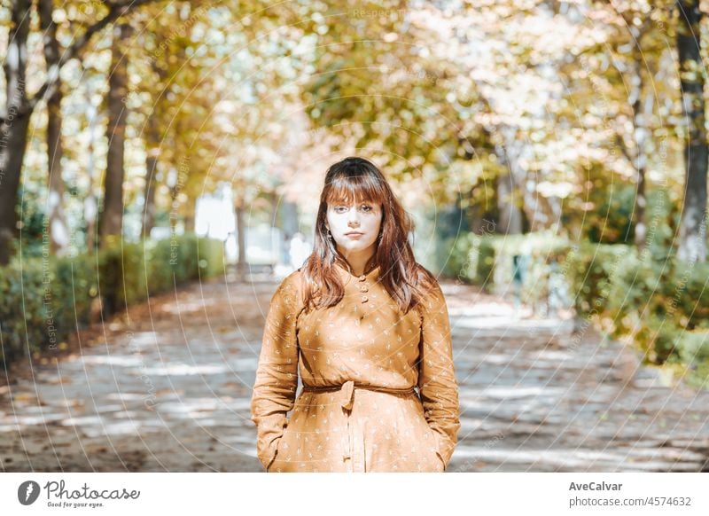 Autumn portrait of a young woman with a hipster dress walks in the park with foliage. Place for text, copy space. Autumnal park. Looking serious to camera