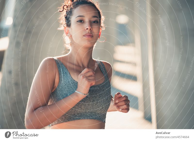 African american young athletic woman, curly hairstyle, running outdoors in the city, corridor Urban sports in the city. Sunset time with shadows. Serious woman concentrating in the competition train.