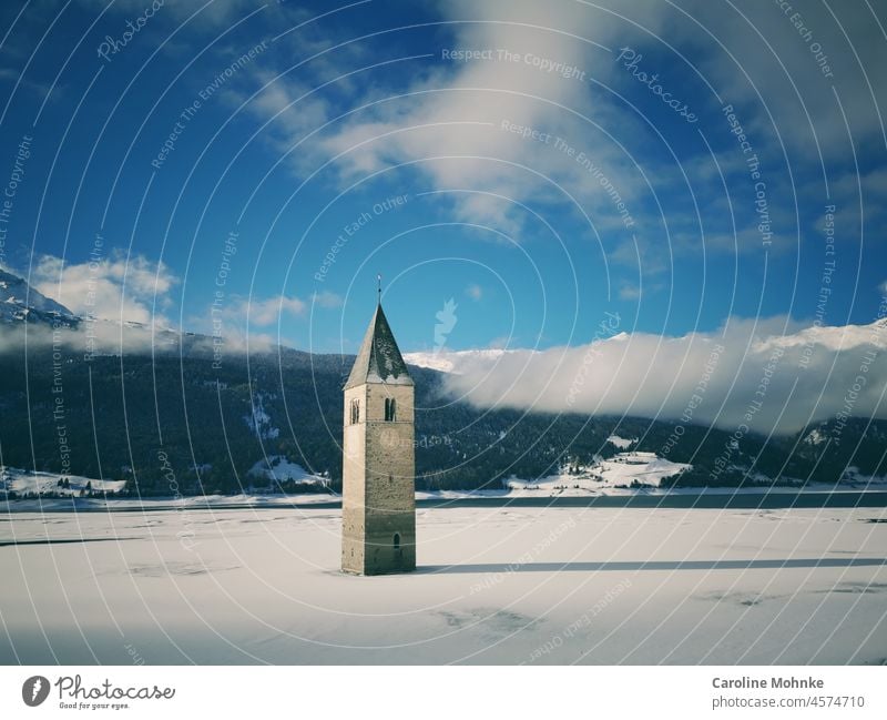Einsam versunkener Kirchturm ragt aus dem teilweise zugefrorenen Reschensee Reschenpass Himmel blau Wasser Wahrzeichen Turm Turm im See märchenhaft faszinierend