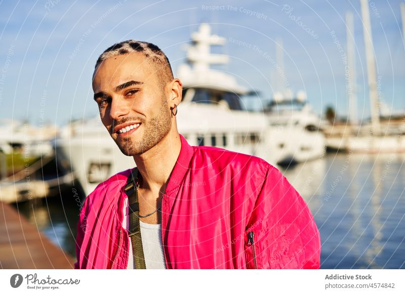Informal man sitting on harbor with boats eccentric cool appearance marina style individuality portrait informal glance male happy unusual haircut trendy gaze