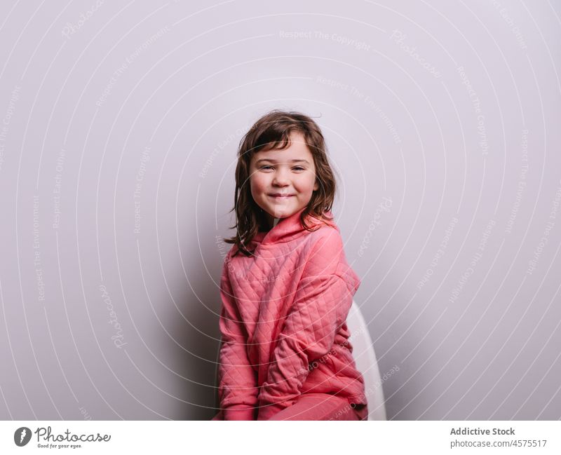 Cheerful girl against gray wall smile chair happy cute appearance sit outfit portrait child cheerful modern kid glad optimist casual childhood adorable rest