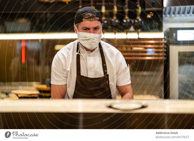 Cook in uniform working in restaurant kitchen man cook protect prepare professional covid job male coronavirus new normal covid 19 mask small business pandemic