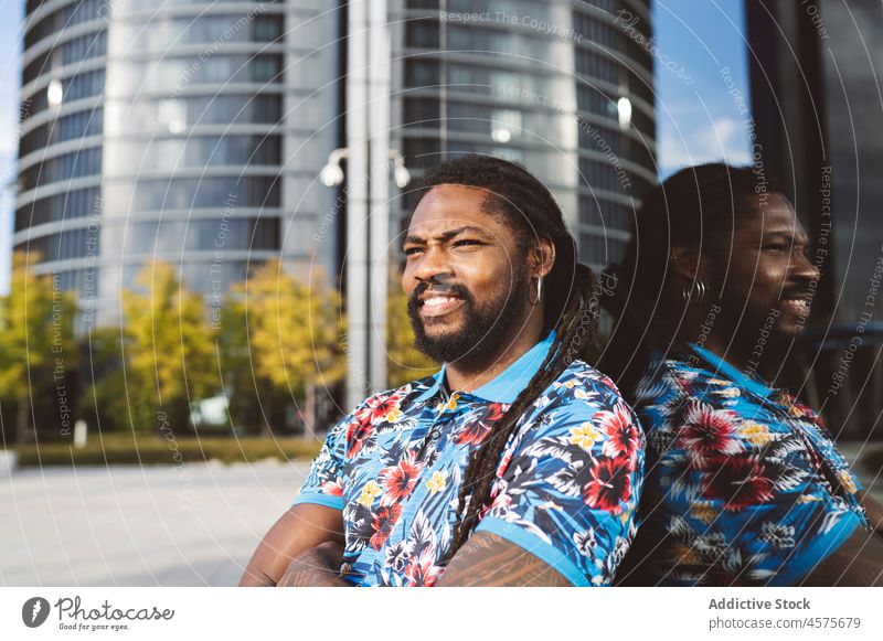 Black man sitting on street near building urban city modern style smile pastime apparel happy outfit reflection male african american black confident beard