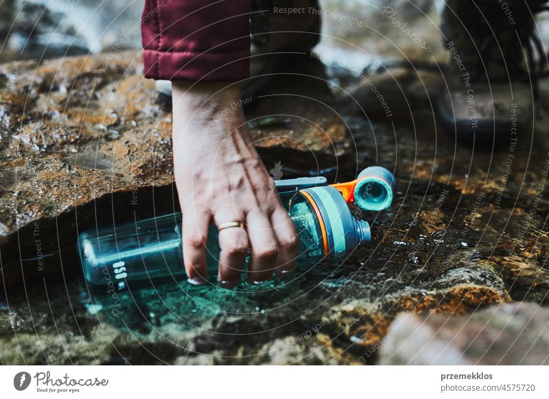 Woman taking pure water to bottle from mountain stream during trekking in mountains adventure trip travel hiking thirsty vacation journey crouching summer