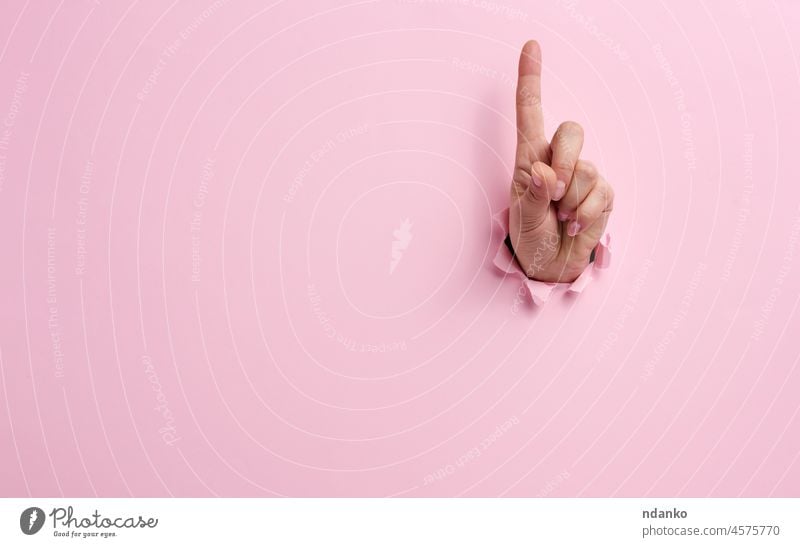 female hand sticking out of a torn hole in a pink paper background, attention gesture adult arm break breakthrough cardboard care caucasian concept