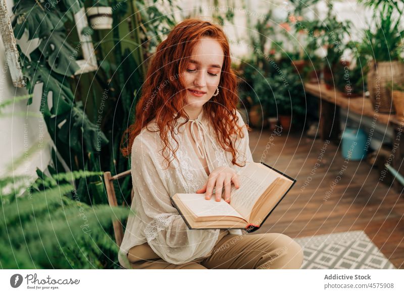 Young woman reading book among potted plants literature leisure pastime hobby garden botany female flowerpot novel concentrate focus redhead chair intellect