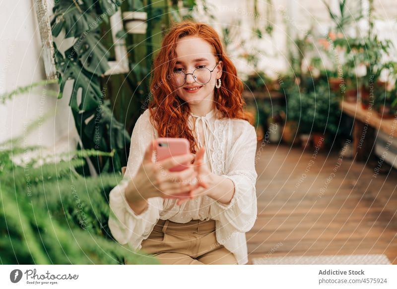 Positive red haired female taking selfie on smartphone woman using botanic grow plant garden positive foliage cellphone botany potted self portrait charming