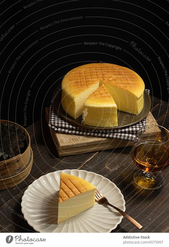 Japanese cheesecake with drink on table whole cake japanese cheese cake dessert food dim plate glass portion appetizing cotton dark obscure timber wooden lumber