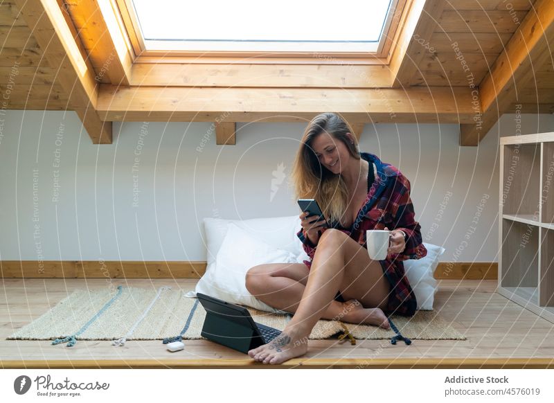 Blogger woman using on mobile phone while sitting on floor smartphone tablet gadget device legs crossed social media coffee bedroom home smile apartment