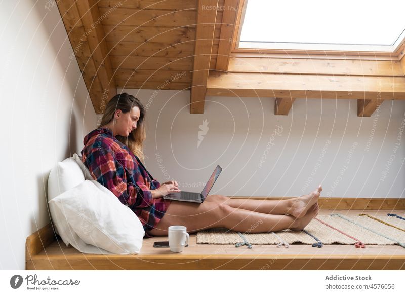 Focused lady using laptop in attic woman typing garret bed browsing rest chill tea independent comfort gadget relax cup blond female lifestyle distance busy