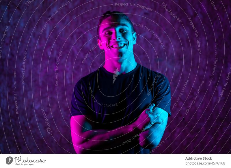 Cheerful male amputee under neon light man smile happy handicap illuminate purple bright portrait young friendly disable positive arms crossed cheerful
