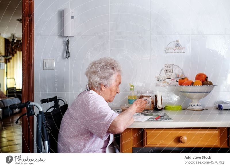 Elderly woman in wheelchair eating in kitchen meal disable handicap pensioner food disease aged female home at home elderly apartment mature gray hair old