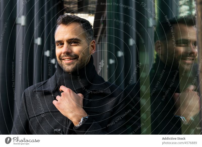 Man standing near black glass of modern building man street confident coat urban trendy male smile style outfit pensive reflection thoughtful city construction