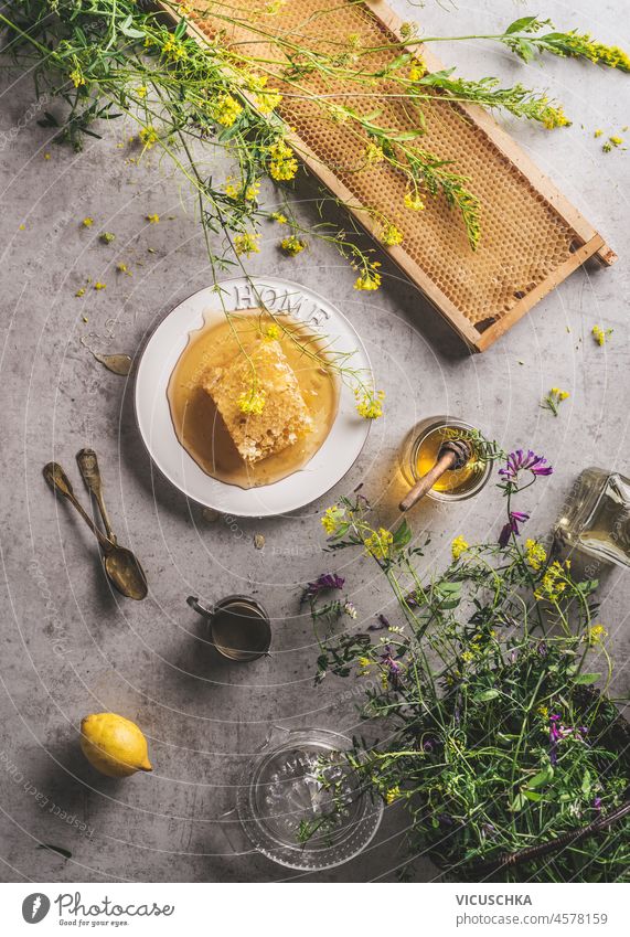 Whole raw honeycomb with honey and honey-dipper, fresh flowers and lemon on grey concrete kitchen table. Natural healthy lifestyle. Top view. whole natural