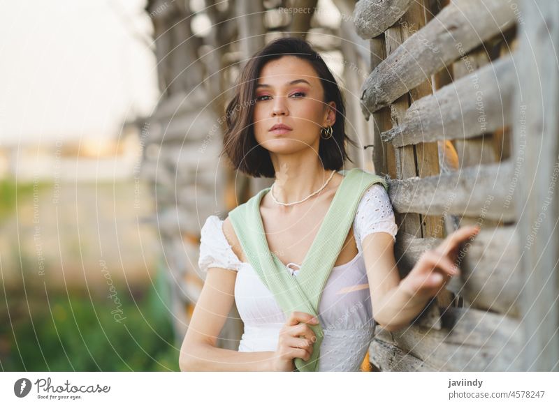 Asian woman, posing near a tobacco drying shed, wearing a white dress and green wellies. countryside female girl pretty people nature fashion lady spring season