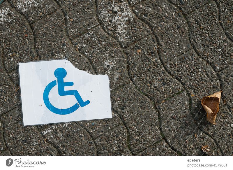 A torn and wet disabled person sign on the ground ableism access accessible asphalt behindertenparkplatz blue concept disability german handicap handicapped