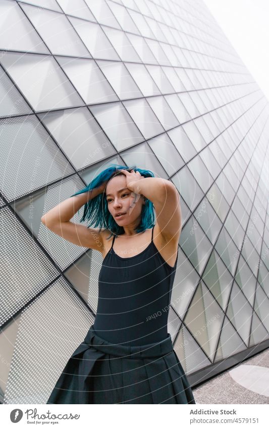 Female with blue hair standing near wall of modern building woman appearance contemporary portrait urban skyscraper trendy street city female outfit style