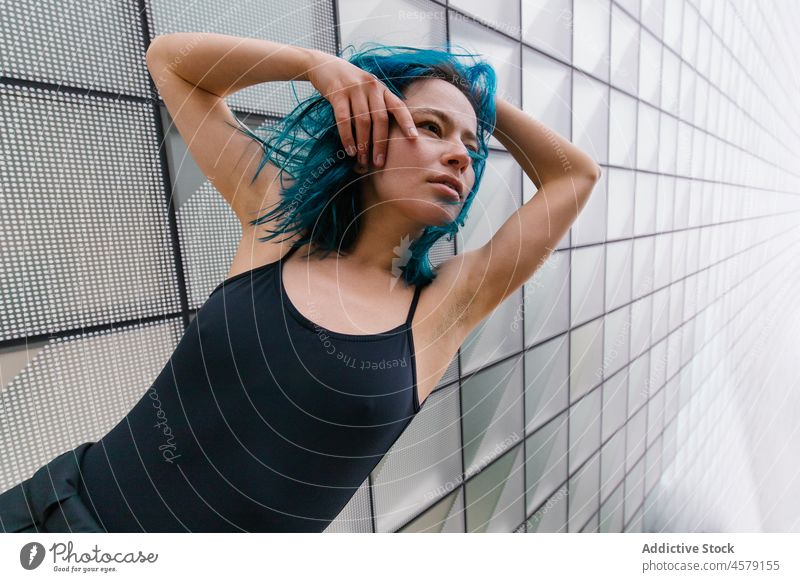 Female with blue hair standing near wall of modern building woman appearance contemporary portrait urban skyscraper trendy street city female outfit style