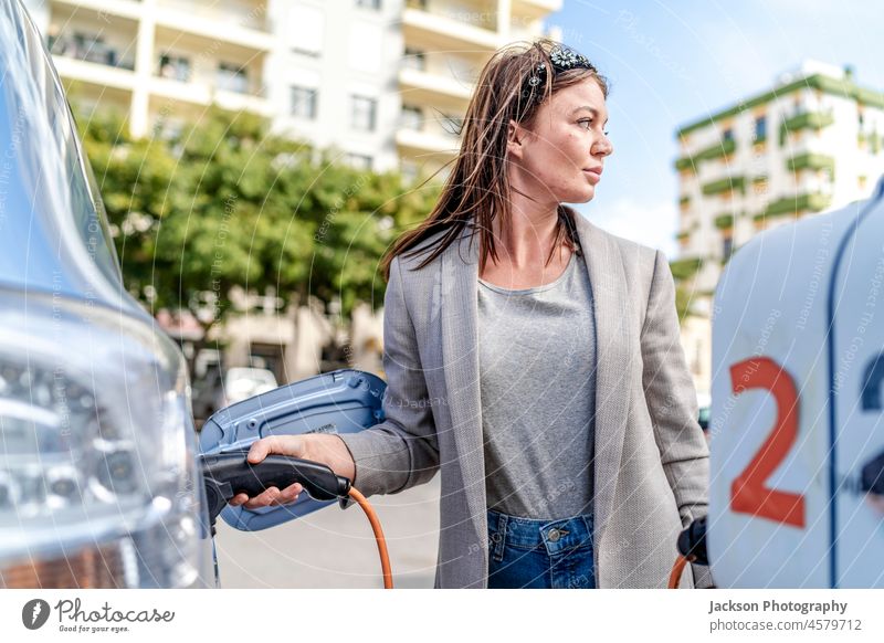 Woman charging an electric car in urban settings. charge woman charging station caucasian renewable energy beautiful young female holding attractive