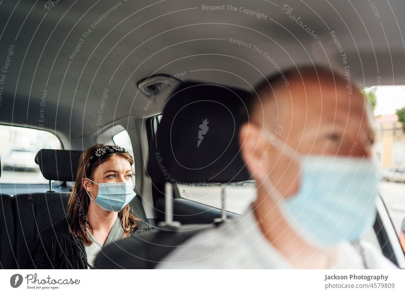 Taxi driver in a mask with a client on the back seat wearing mask uber taxi car passenger caucasian travel woman distance ride protect surgical mask viral adult