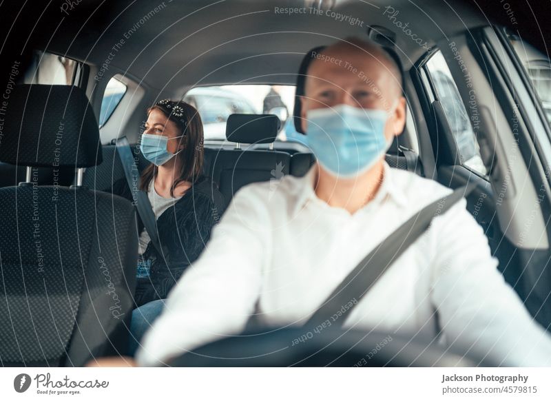 Taxi driver in a mask with a client on the back seat wearing mask uber taxi car passenger caucasian travel woman distance ride protect surgical mask viral adult