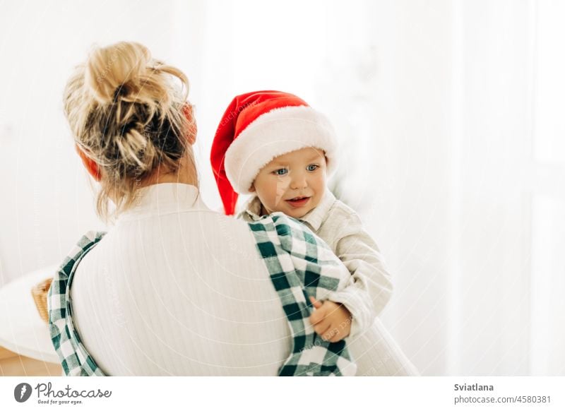 A blonde woman holds her little son in a Santa costume in her arms. The concept of Christmas and New Year baby mother santa suit holding christmas family new