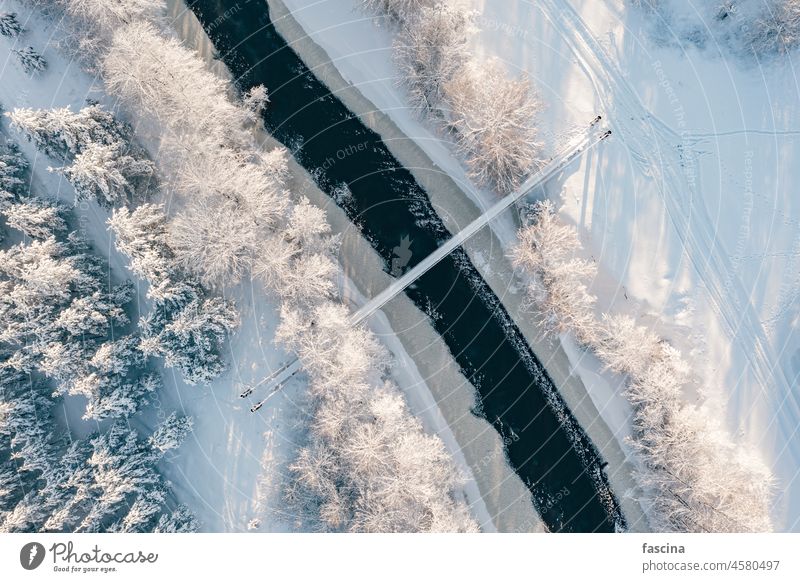 Drone shot frozing small river, suspension bridge birds-eye winter scene view ice forest freezing snow covered sunny day drone frozen north landscape aerial