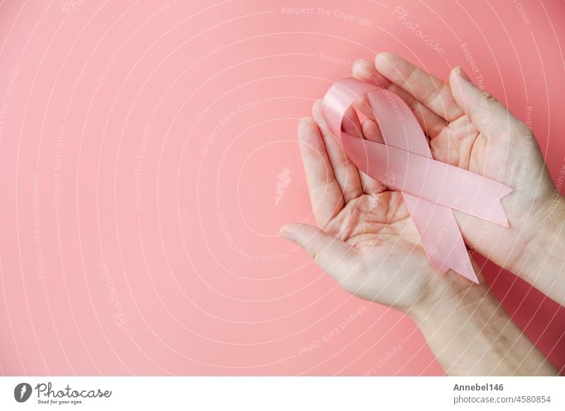 Female hands holding pink ribbon over pink background, breast cancer awareness, October pink concept top view with copy space, health, woman cancer concept care