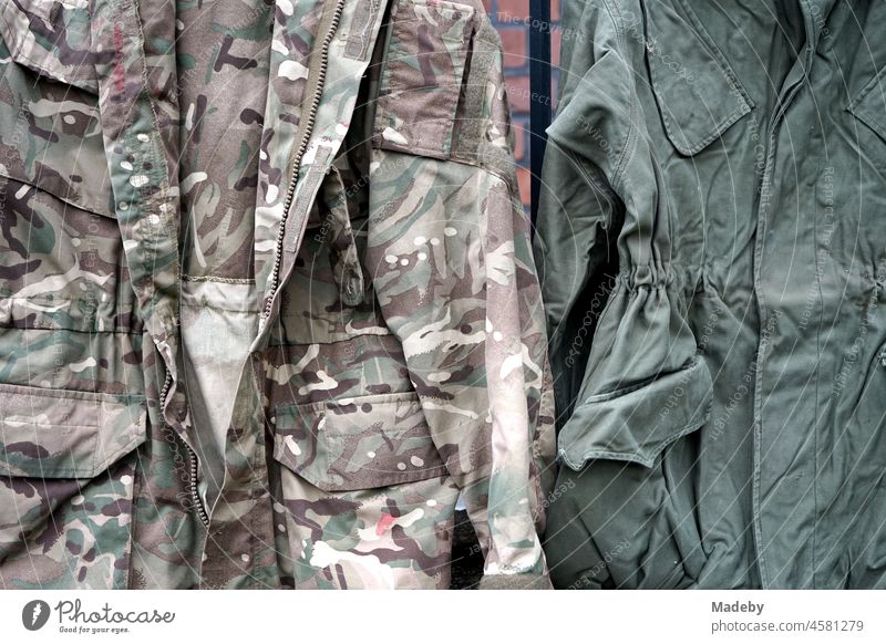 Old military jackets in olive and camouflage colours with camouflage pattern on the brick wall in front of an old factory in the Margaretenhütte district of Giessen on the river Lahn in the German state of Hesse
