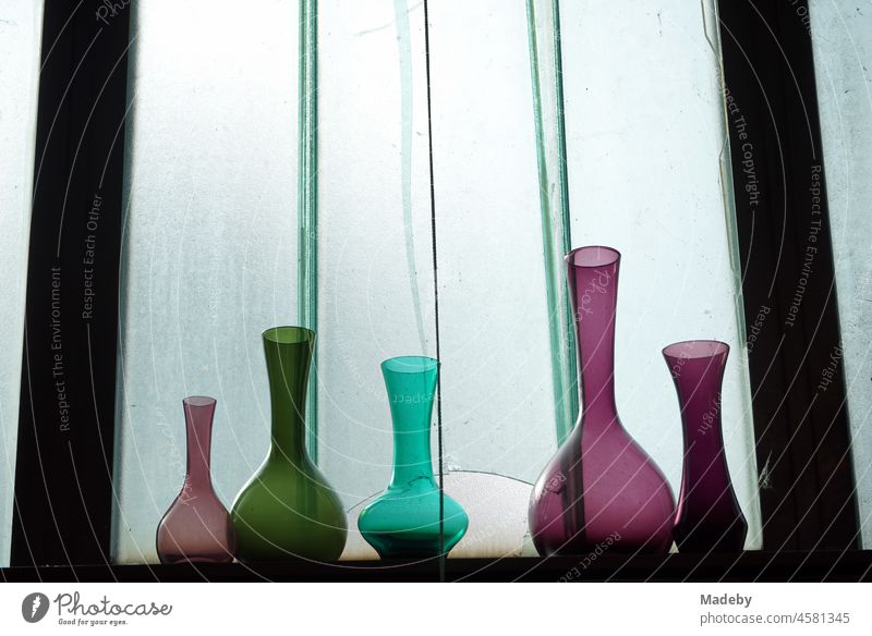 Coloured vases and flasks made of glass on a shelf in front of the window pane of an old factory building in the Margaretenhütte district of Gießen on the Lahn in Hesse
