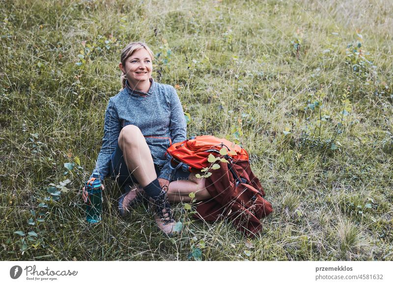 Smiling happy woman with backpack resting on grass during a hike in the mountains summer trip active adventure activity fun travel trekking vacation female