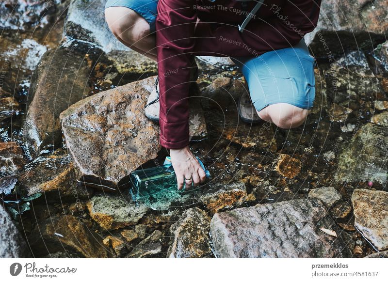 Woman taking pure water to bottle from mountain stream during trekking in mountains adventure trip travel hiking thirsty vacation journey crouching summer