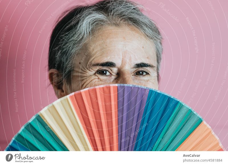 Old senior white hair woman holding an lgbti hand fan colourful background. Old people senior concept. Woman rights lgbt friendly purple background celebrate