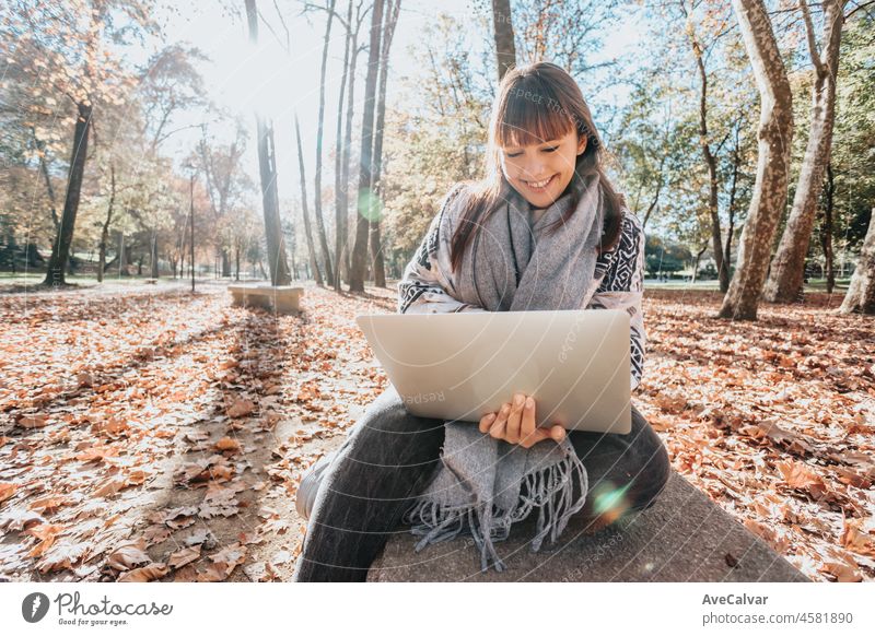 Young streamer caucasian girl outside using a laptop to check work, happy and smiling attitude. Young and modern trendy style. Autumnal season. Working anywhere, financial freedom, investments