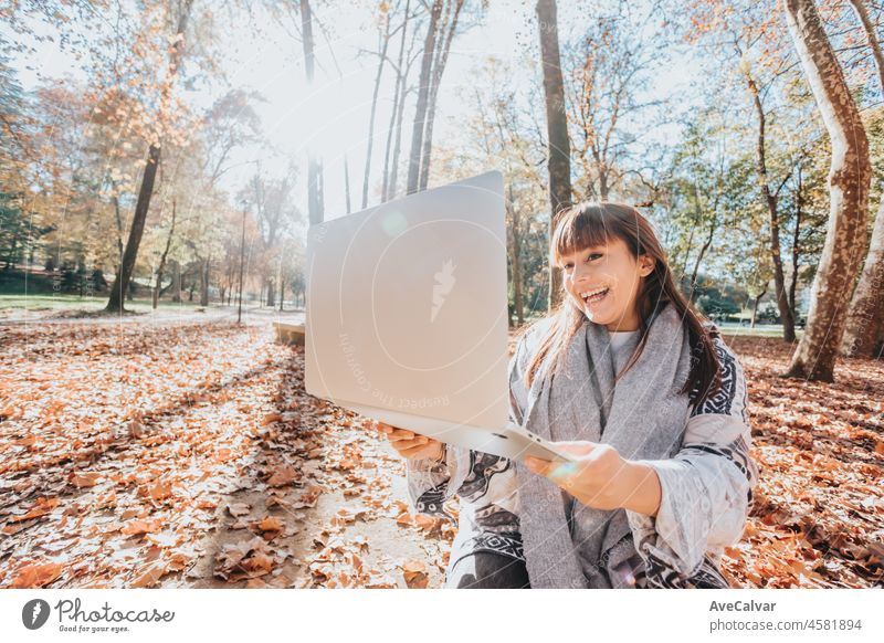 Young streamer caucasian girl outside using a laptop to check work, happy and smiling attitude. Young and modern trendy style. Autumnal season. Working anywhere, financial freedom, investments
