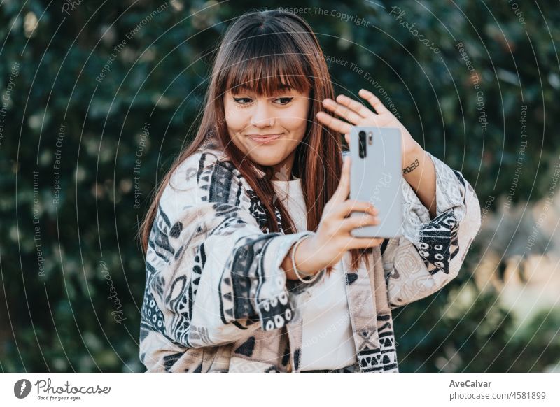 Young streamer caucasian girl outside using a smart phone to stream, happy and smiling attitude. Young and modern trendy style. Autumnal season. Working anywhere, social networks
