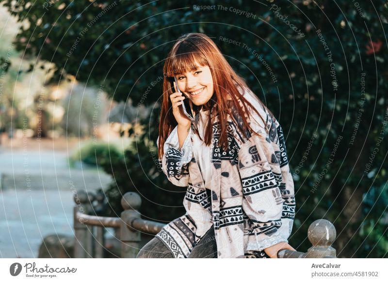 Young streamer Young woman in the park during a phone call smiling receiving good news on trendy and modern clothes with copy space to add your advertisement or copy text.Blurred background confidence towards future girl outside using a laptop to check ...
