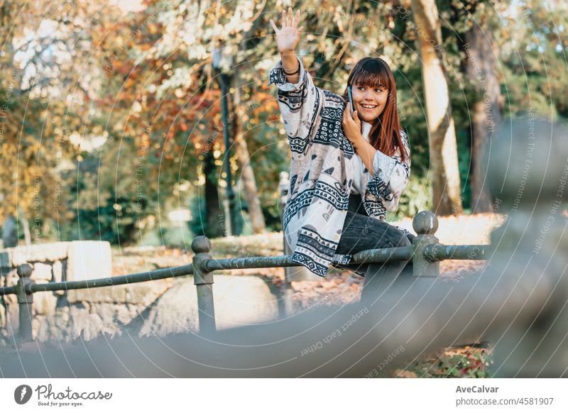 Young woman in the park during a phone call smiling receiving good news and saluting waiting for his friends to come and saluting them with copy space to add your advertisement or copy text.