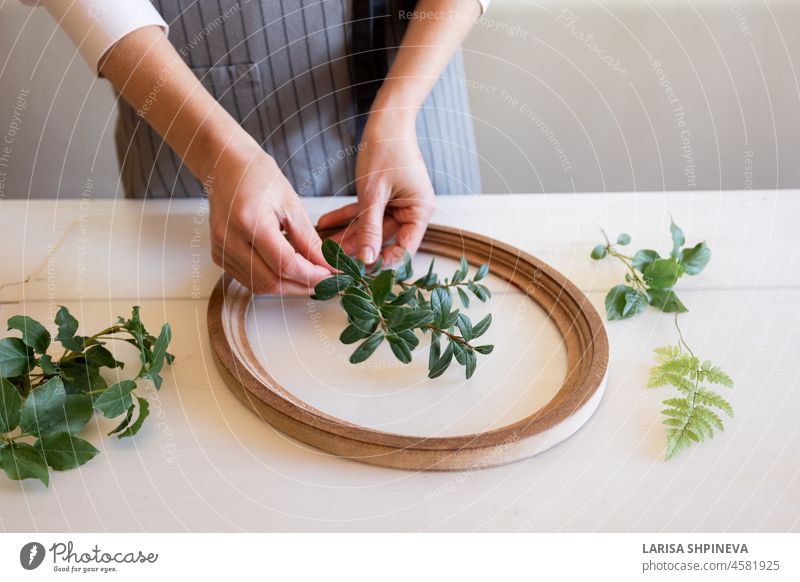 Woman puts branches of plants into frame for making botanical bas-relief. Female hands for working with clay, plasticine on desktop, top view art craft wooden