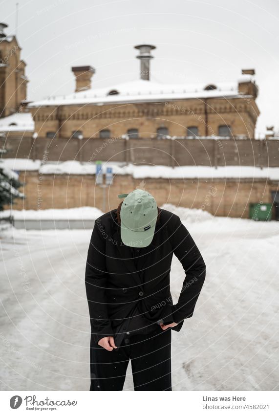 It’s cold outside. Wintertime. A woman dressed in a black suit and green cap is wandering in the city. The location is Vilnius, Lithuania. winter snow