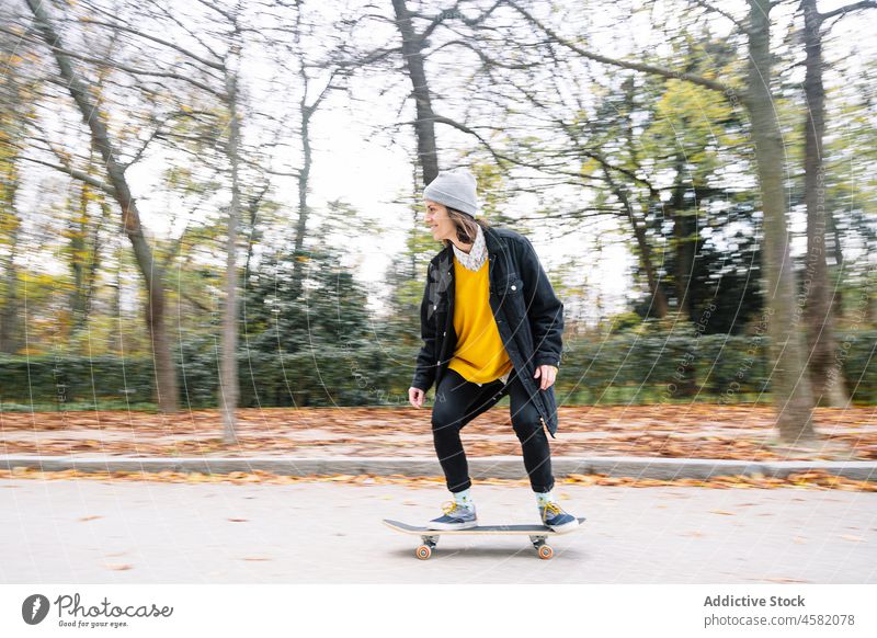 Young female skater riding skateboard in autumn park woman ride cheerful hobby defocused happy road asphalt casual young nature energy activity longboard smile