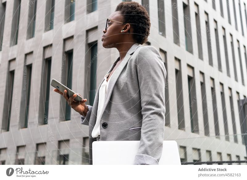 Black female entrepreneur with laptop ans mobile phone in street near office building woman device smartphone netbook african american businesswoman formal